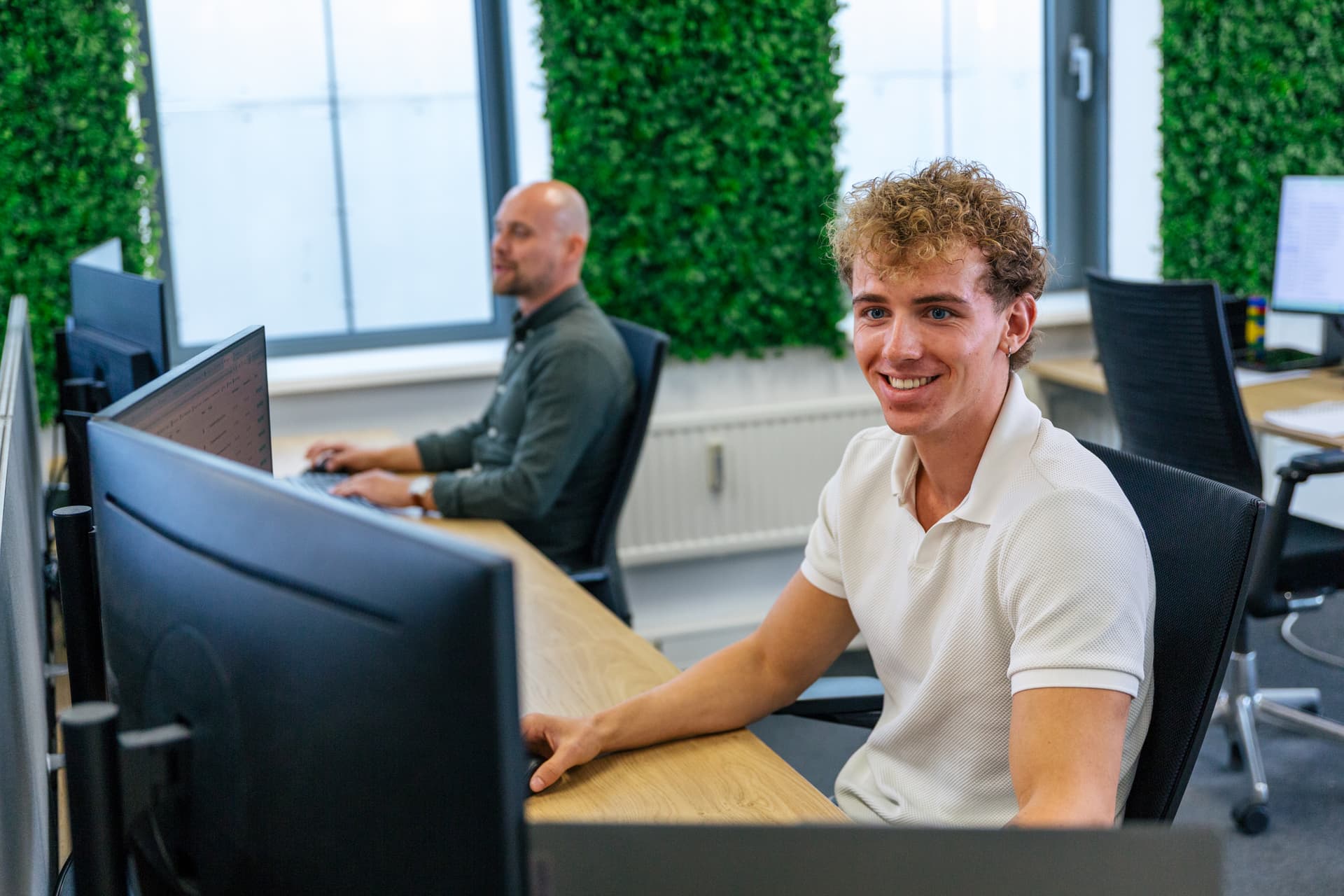 Jonge collega van Prosperos lacht vanachter zijn bureau op kantoor