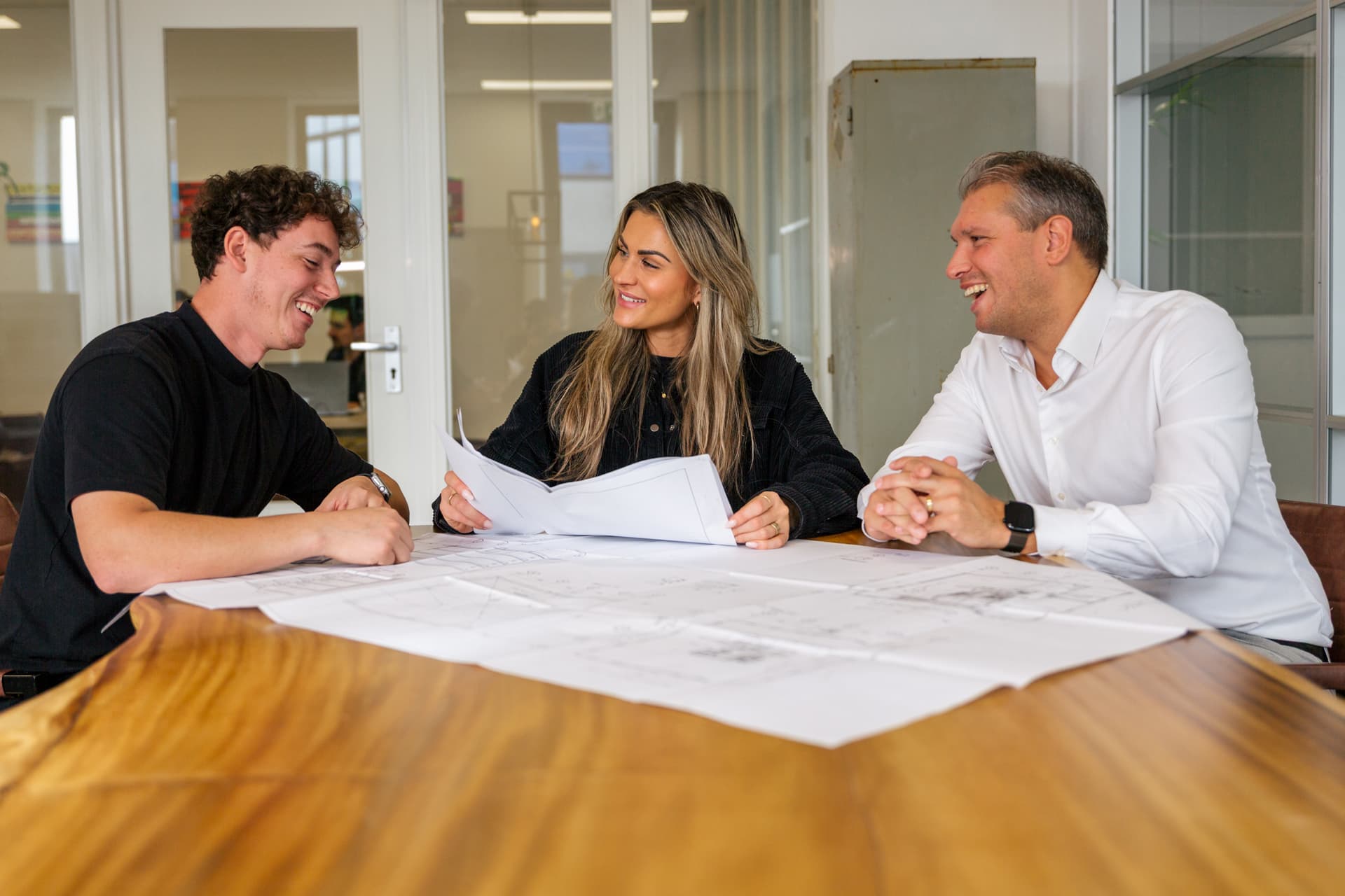 Drie collega's van Prosperos bespreken samen bouwtekeningen aan een tafel op kantoor