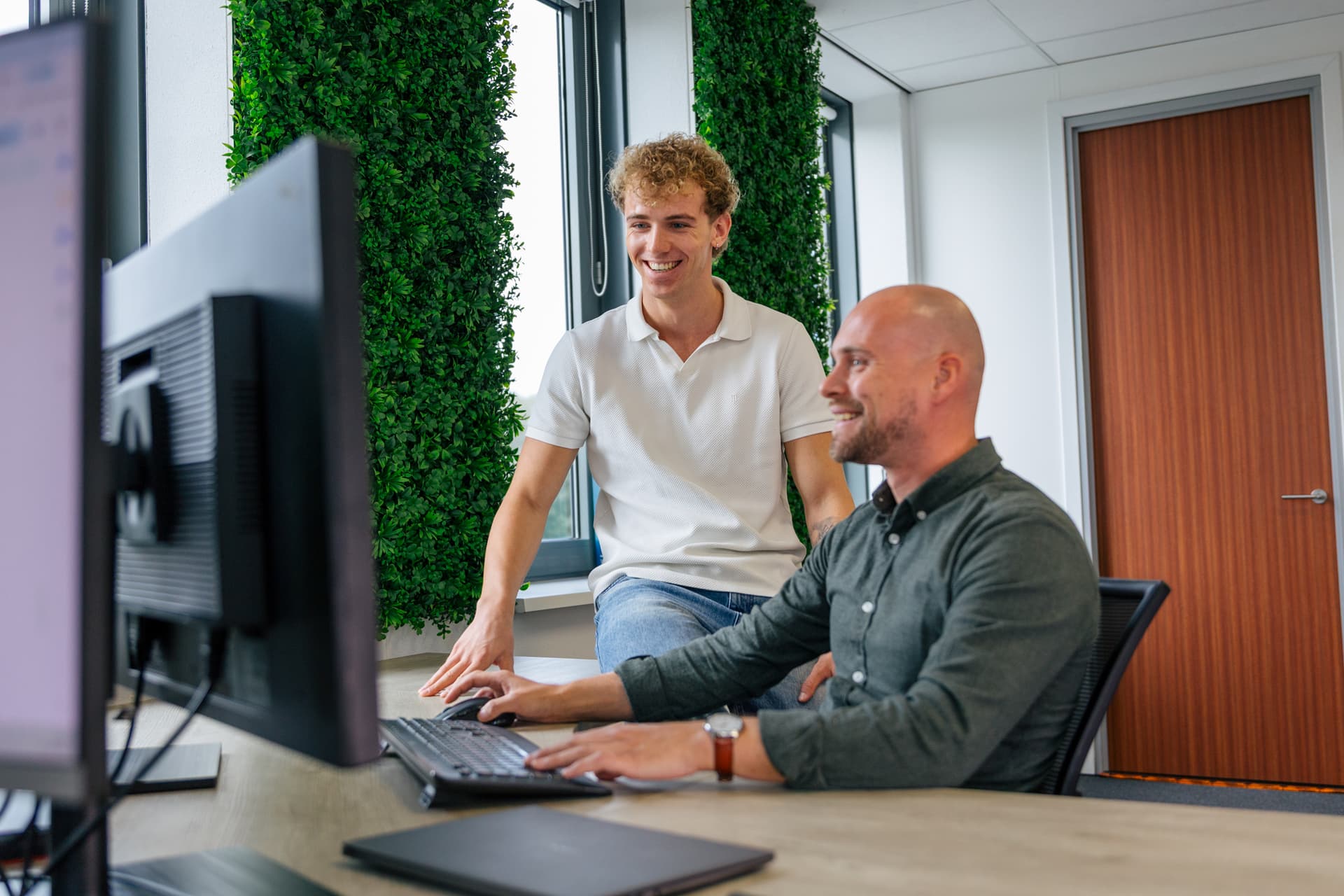 Ervaren collega legt een jonge collega iets uit achter de computer