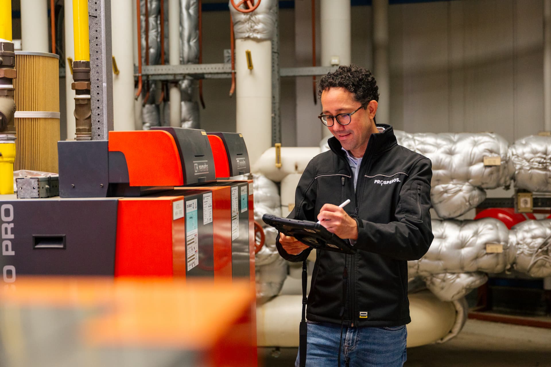 Energieprestatieadviseur van Prosperos noteert gegevens op een tablet in een ketelruimte